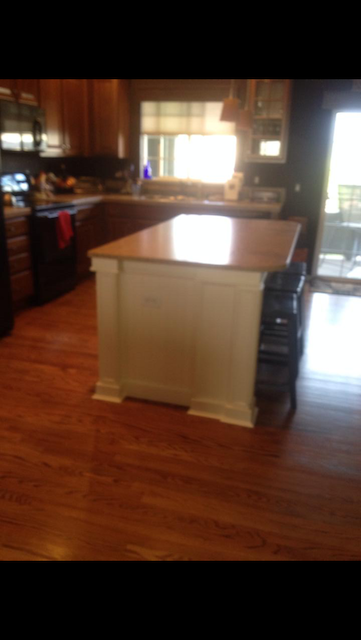 Kitchen island with white base, wood countertop, and dark floor. Window and sliding door in background.