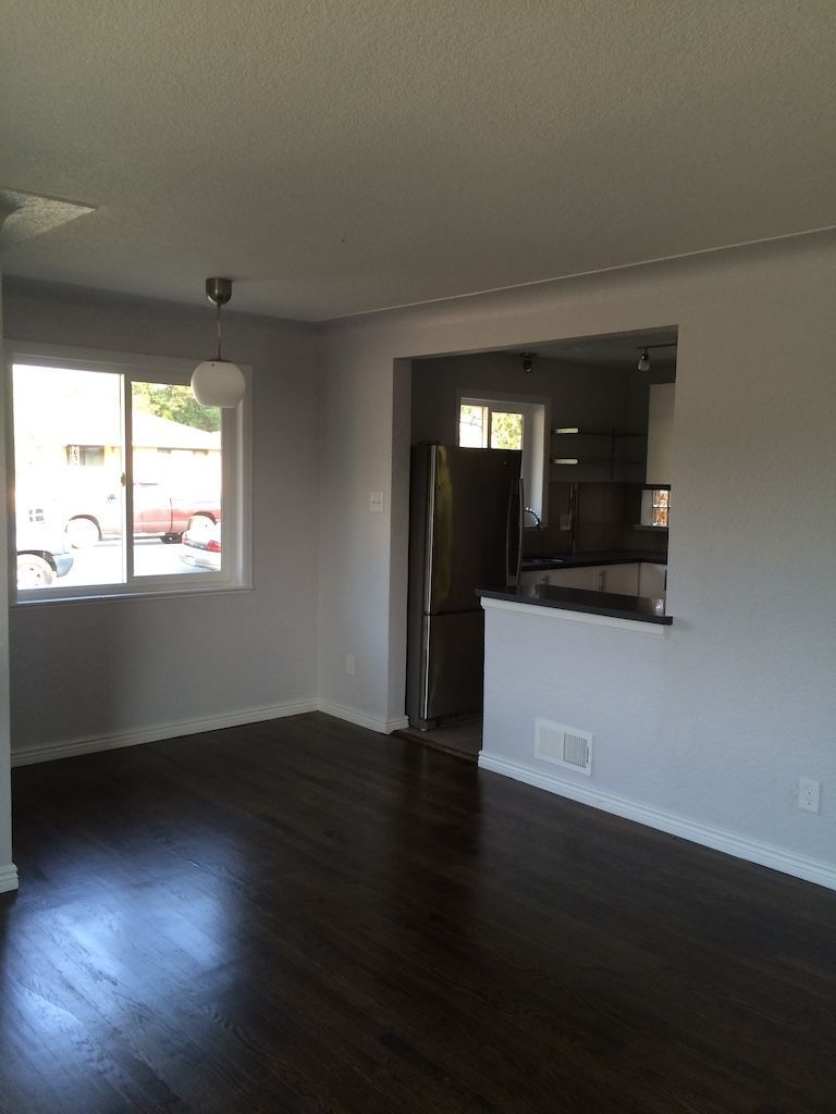 Dark-floored room with a window and an opening to a kitchen, painted in gray and white.