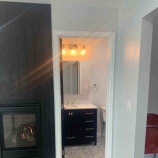 A dark blue bathroom vanity with a white countertop and a herringbone tiled wall with a fireplace.