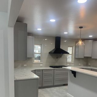 Modern kitchen with gray cabinets, white countertops, black range hood, and pendant light.