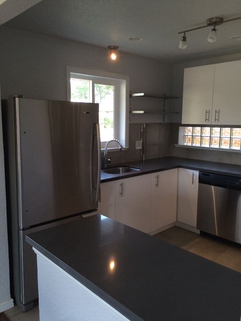 Modern kitchen with stainless steel appliances, white cabinets, dark countertops, and a small breakfast bar.