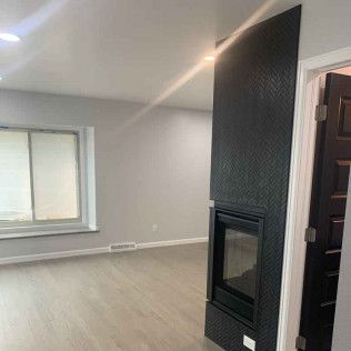 Modern living room with fireplace and light-colored flooring, next to a doorway with a dark door.