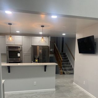 Modern kitchen with stainless steel appliances, gray cabinets, and a breakfast bar. A TV is on the adjacent wall.