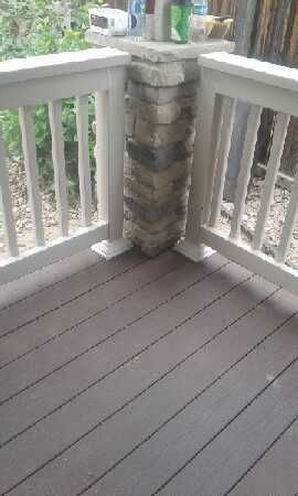 Deck corner with stone pillar and light-colored railing. Brown composite decking.