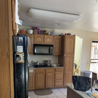 Kitchen with wooden cabinets, a microwave, and a refrigerator. A large light fixture is on the ceiling.