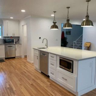 Modern white kitchen with a stainless steel dishwasher and microwave. Hardwood floors and brass pendant lights.