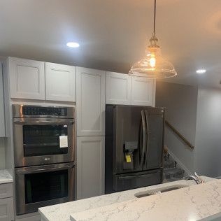 Kitchen with stainless steel double oven, gray refrigerator, white cabinets, and a pendant light.