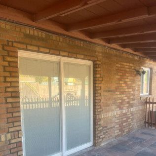 Sliding glass door and small window in a brick exterior wall. Brown wooden beams form a porch.