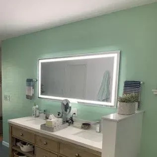 Bathroom with large mirror, green walls, double sink vanity, and towel racks.