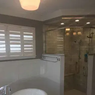 Bathroom with white tub, shutters, glass shower, and gray walls.