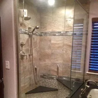 Glass-enclosed shower with tiled walls and a bench seat. Chrome fixtures and glass shelving are present.