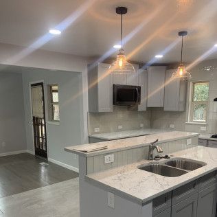 Kitchen with gray cabinets, island with sink, and pendant lights.