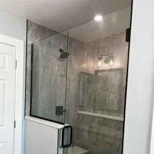Glass shower enclosure with black hardware and gray tile walls.