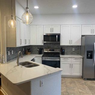 Modern white kitchen with stainless steel appliances and light quartz countertops.
