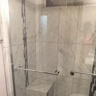 Shower stall with marble-patterned tile, glass door, and chrome hardware.