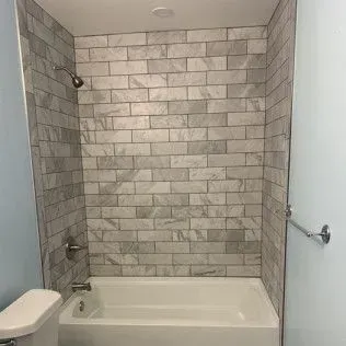 Bathroom with a white bathtub and grey tiled shower walls.