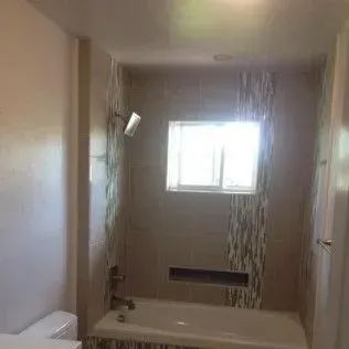 Bathroom with a tiled shower, bathtub, and window.