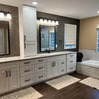 Bathroom with white cabinets, dark tile wall, countertops, mirrors, and a tub.