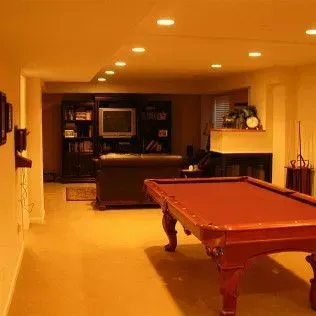 A red pool table in a dimly lit basement, with a television and bookshelf in the background.