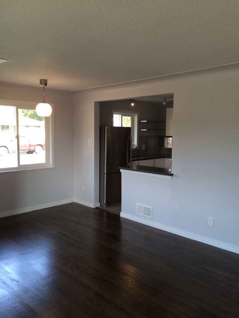 Living room with dark wood floors, light gray walls, and a view into a kitchen area.
