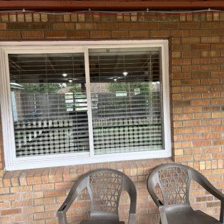 Window with white frame, brick wall, two gray chairs. Blinds inside window.