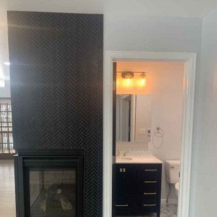 Dark tiled fireplace next to an open doorway to a bathroom with vanity and mirror.
