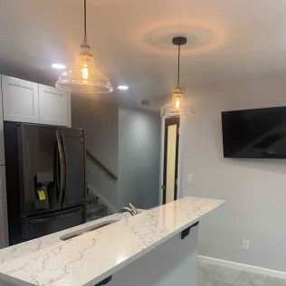 Kitchen with pendant lights over a countertop, a black refrigerator, and a mounted TV.
