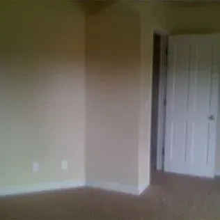 Empty room with beige walls, white door and trim, and brown carpet.