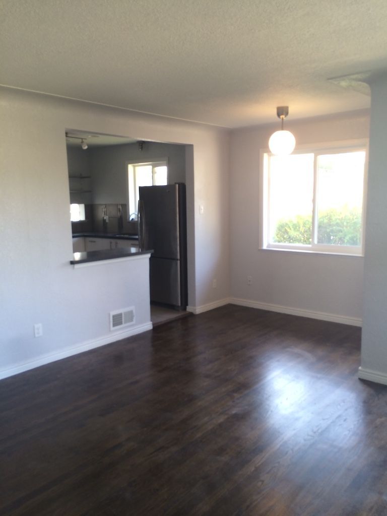 Interior view of dining room with dark wood floor, light gray walls, and open kitchen entrance.