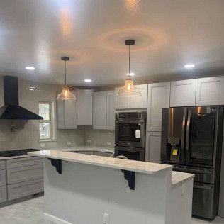 Modern kitchen with gray cabinets, island, black appliances, and pendant lights.