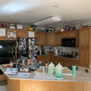 A cluttered kitchen with wooden cabinets, appliances, and an island counter.