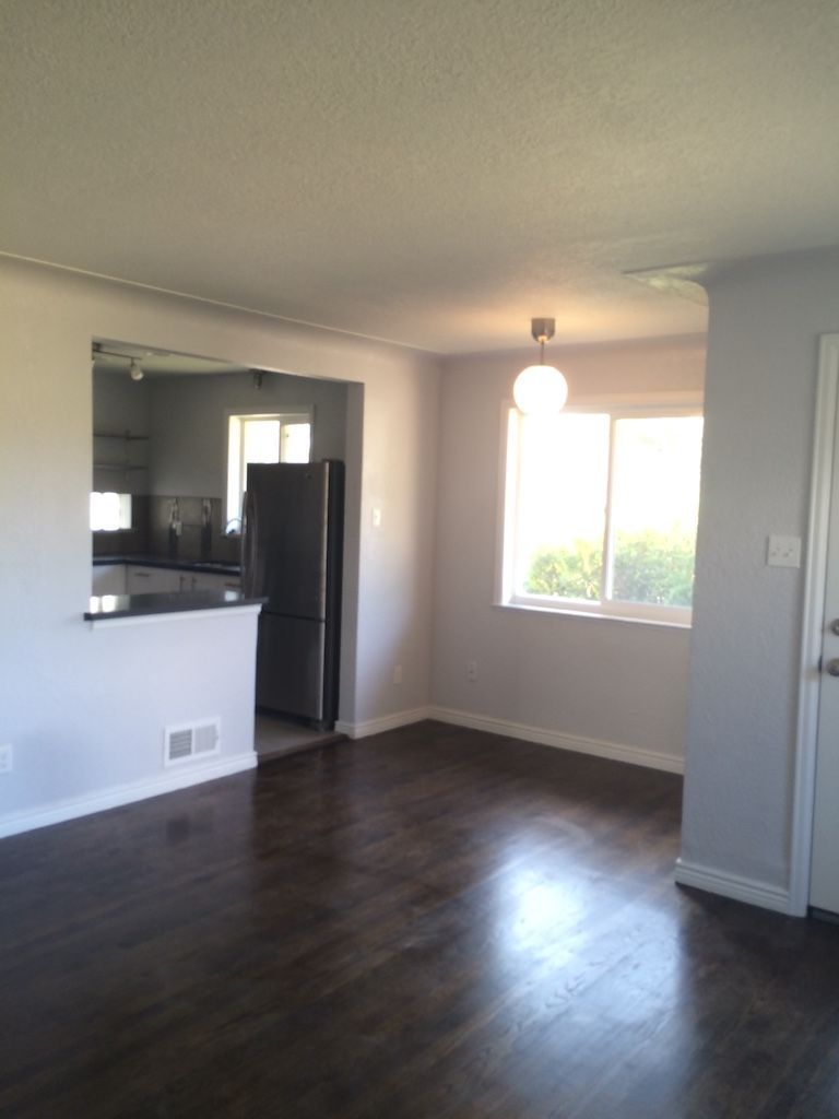 Dining area with dark hardwood floors, gray walls, and a view into a kitchen with a stainless steel refrigerator.
