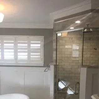 Bathroom interior with a glass shower, white shutters, and gray walls.