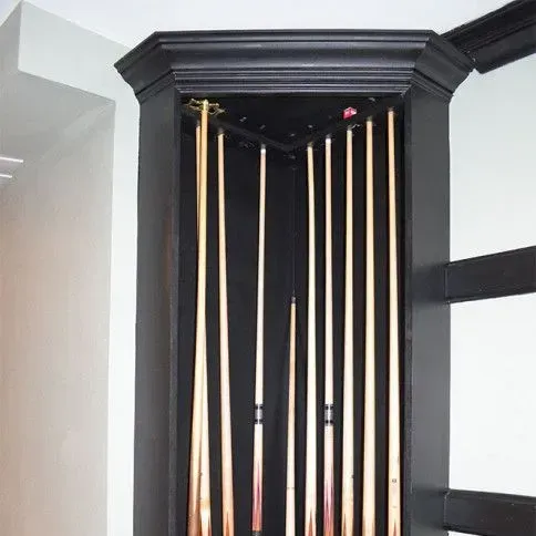 Black corner cabinet holding pool cues, with a white wall in the background.