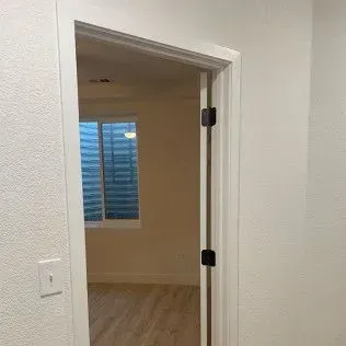 A doorway with a partially open door, revealing a room with a window and wood flooring.