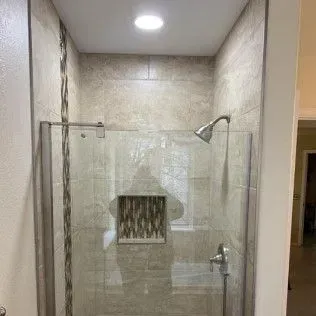 Shower with glass door, beige tile, and silver fixtures.