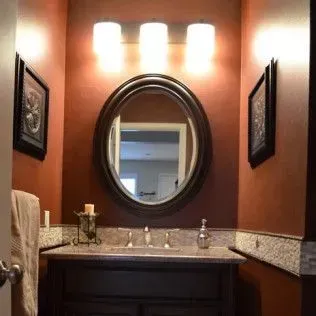 Small bathroom with an oval mirror, sink, and decorative wall sconces. Reddish-brown walls and dark cabinet.