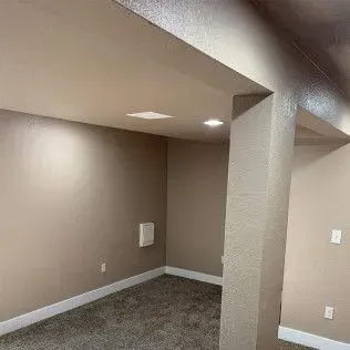 Beige-painted interior room with carpet and a structural pillar. Recessed lights are in the ceiling.