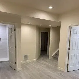 Interior view of a remodeled basement with light-colored walls, doors, and flooring, and recessed lighting.