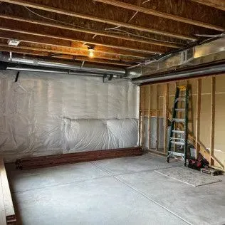 Unfinished basement with concrete floor, wood framing, and insulation. Ladder and construction materials are present.