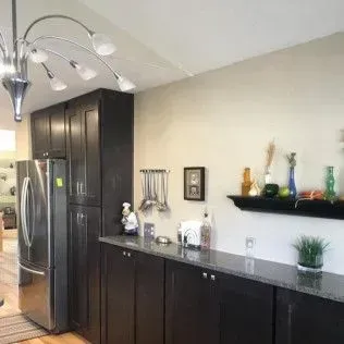 Kitchen with dark cabinets, stainless steel refrigerator, and decorative shelf.