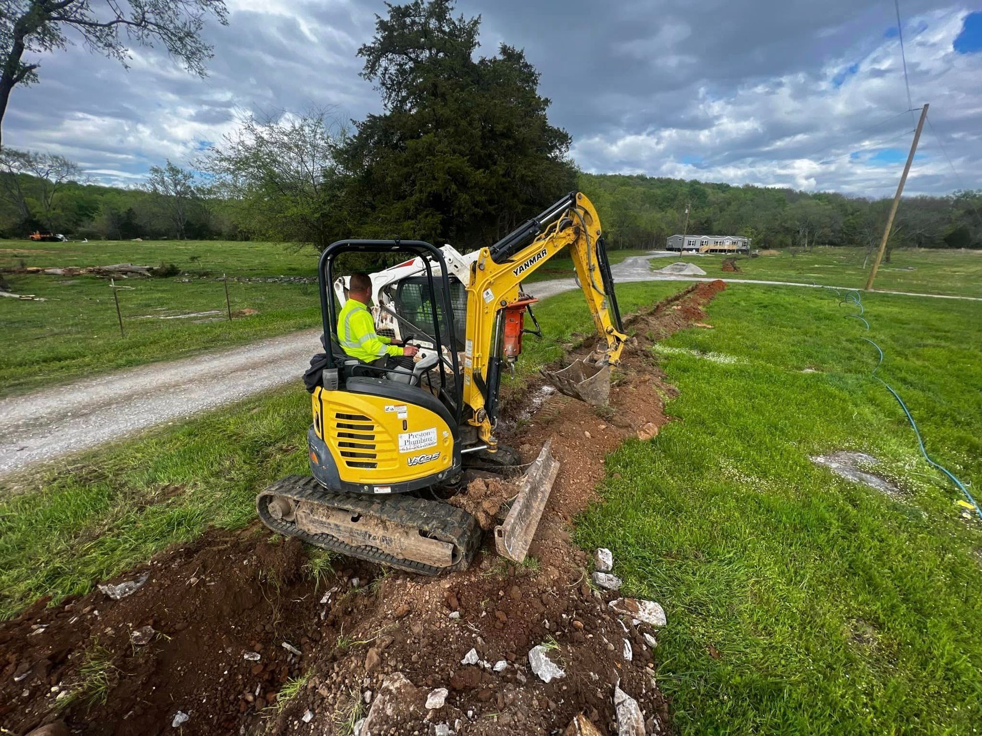 A man is driving a small excavator in a field.