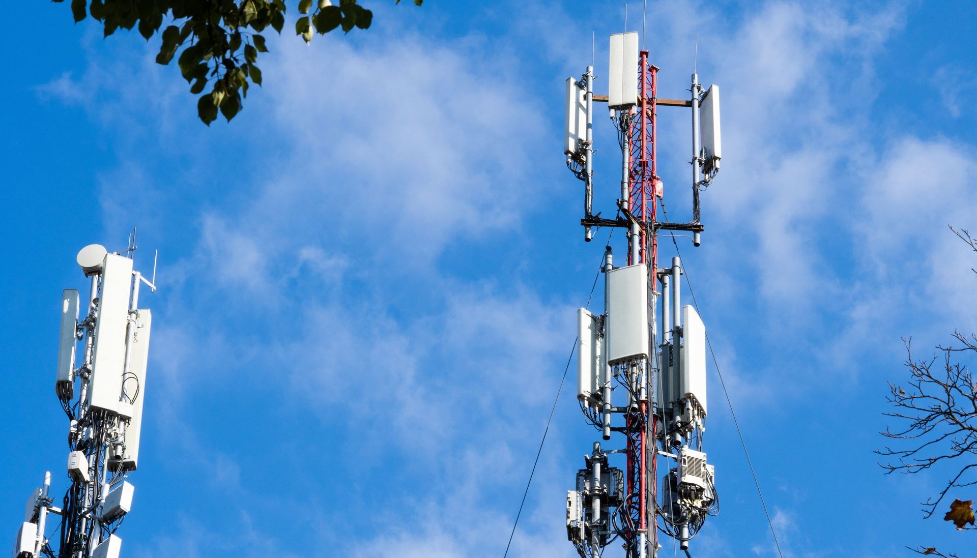 Two cell phone towers against a blue sky with clouds