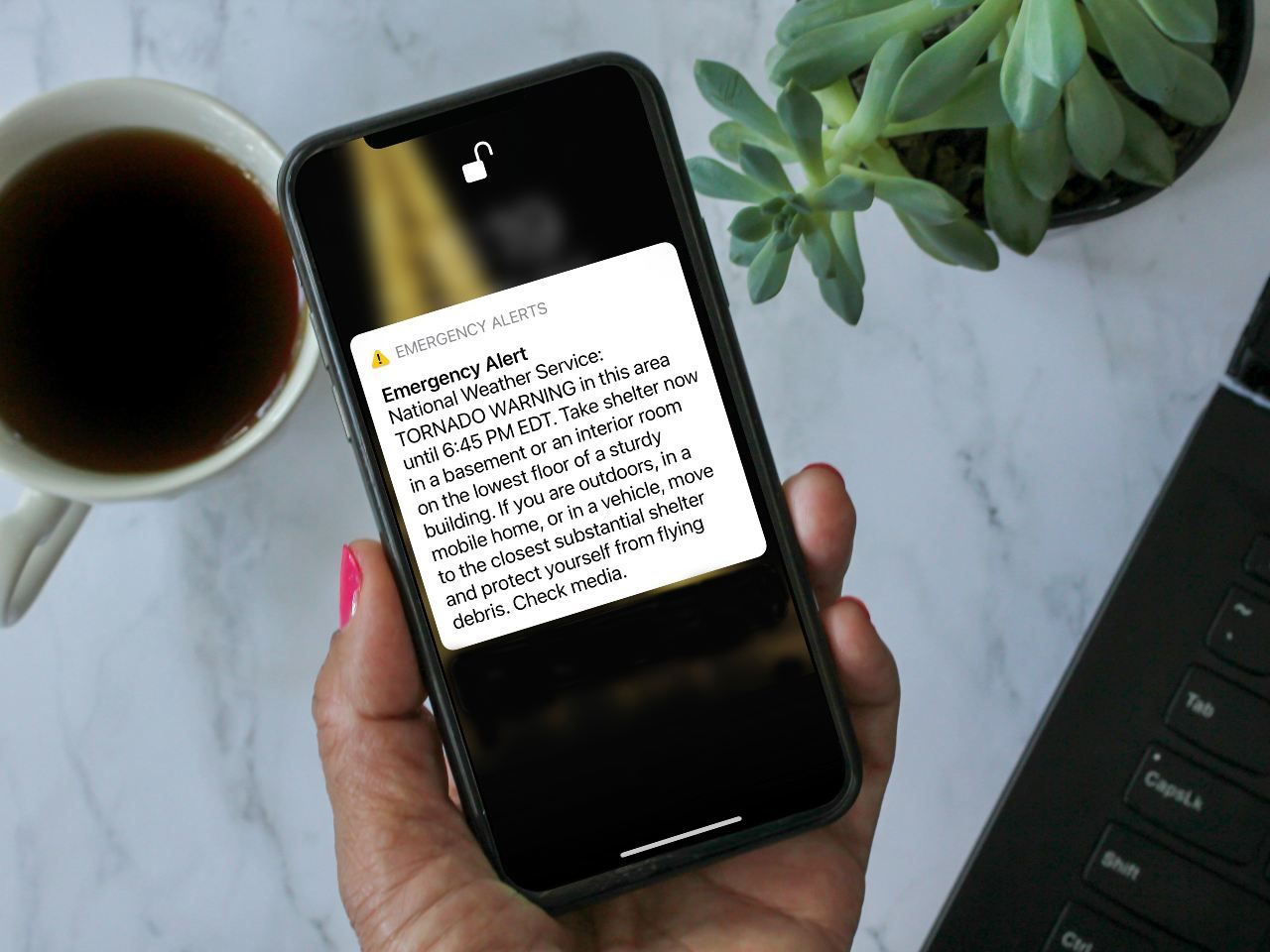 A person is holding a cell phone next to a cup of coffee.