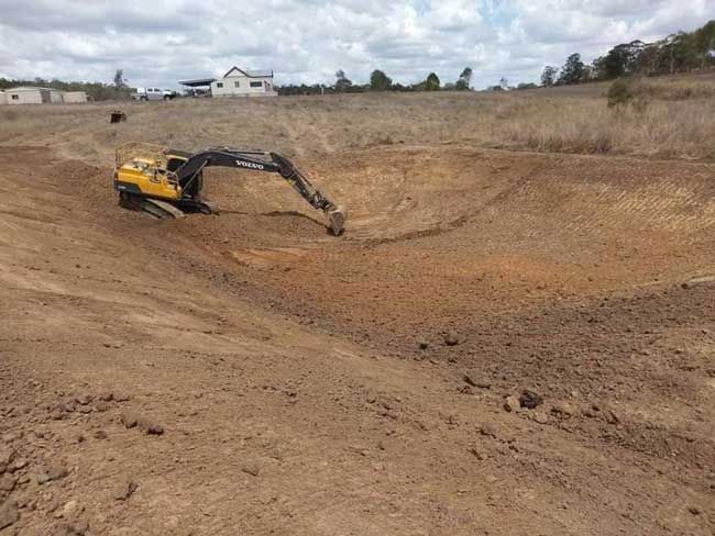 A Yellow Excavator is Digging a Hole in a Dirt Field — A & B Mullins Excavations Pty Ltd in Bundaberg, QLD