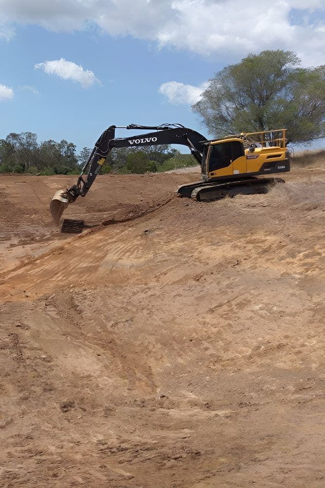 A Yellow Excavator is Moving Dirt in a Field — A & B Mullins Excavations Pty Ltd in Bundaberg, QLD