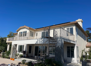 Two-story cream house with white balcony and gray roof under a clear blue sky