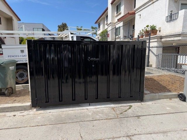 Black metal gate across a residential driveway with white buildings and blue sky behind it