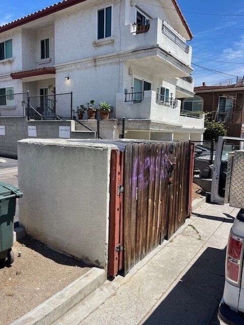 Residential street with a white two-story house, metal gate, and parked car in bright sunlight