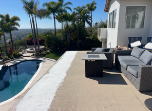 Patio with gray outdoor sofa beside a pool, palm trees, and a hillside view